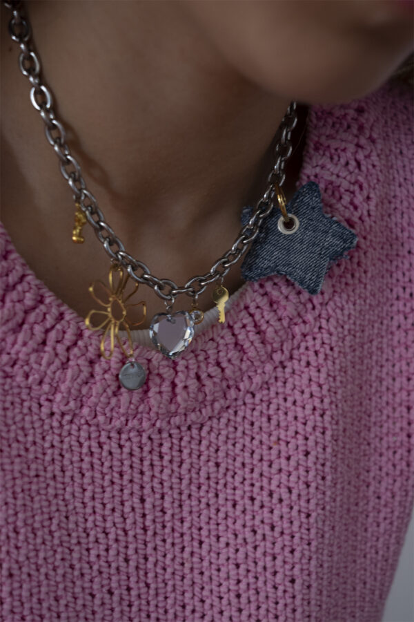 Collier en acier inoxydable. Il s'agit d'un composé d'une chaine argenté, et de multiples pendentifs doré aux formes diverses en acier, cristal et jean