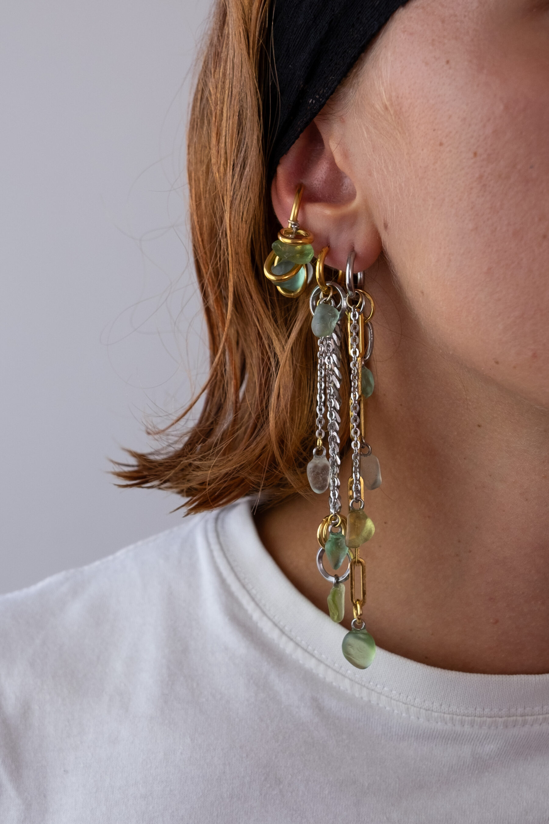 Mono boucle d’oreilles en acier inoxydable composée d’une créole doré ou argenté, et de morceaux de verre poli ramassés sur les plages du sud de la France disposés sur des chaines de tailles différentes pour un rendu en cascade.