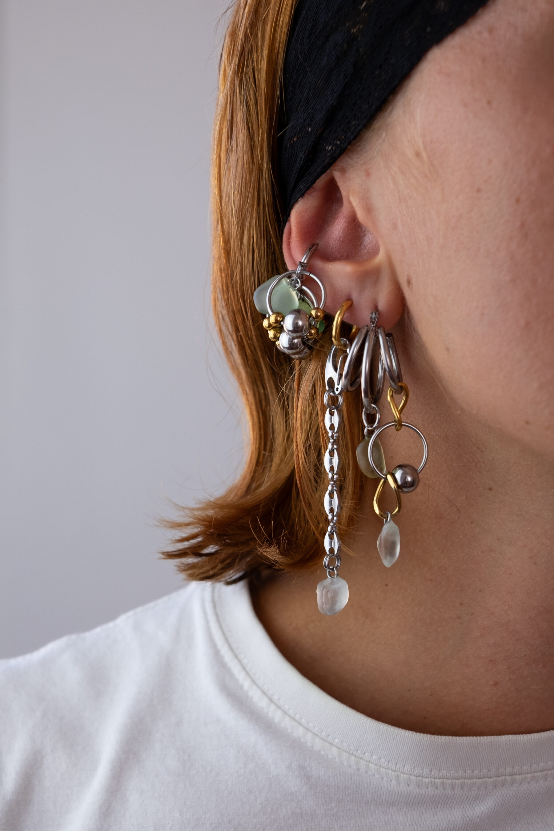 Mono boucle d’oreilles en acier inoxydable composée d’une créole doré ou argenté, et de morceaux de verre poli ramassés sur les plages du sud de la France disposés sur des chaines de tailles différentes pour un rendu en cascade.