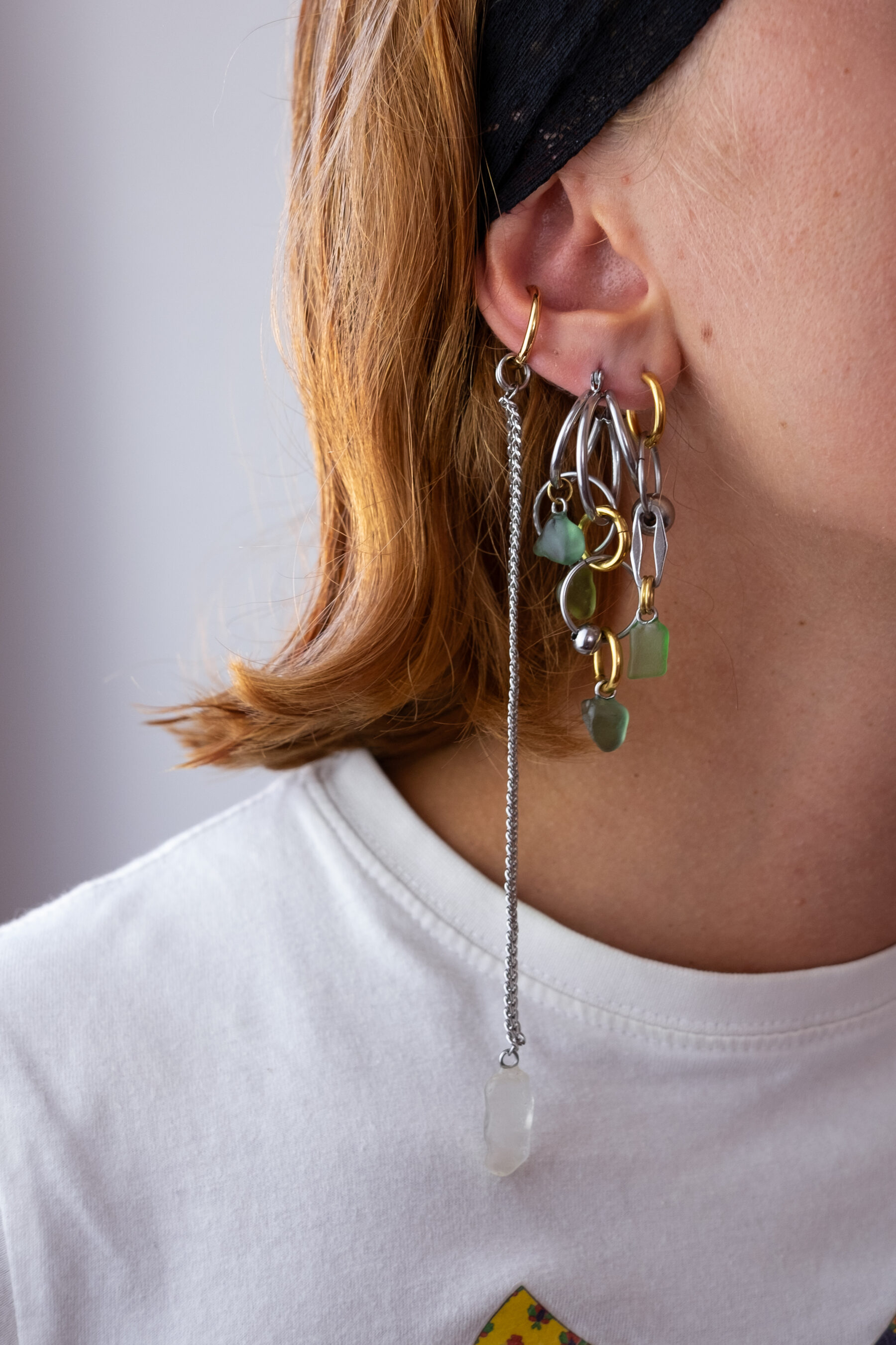 Mono boucle d’oreilles en acier inoxydable composée d’une créole doré ou argenté, et de morceaux de verre poli ramassés sur les plages du sud de la France disposés sur des chaines de tailles différentes pour un rendu en cascade.