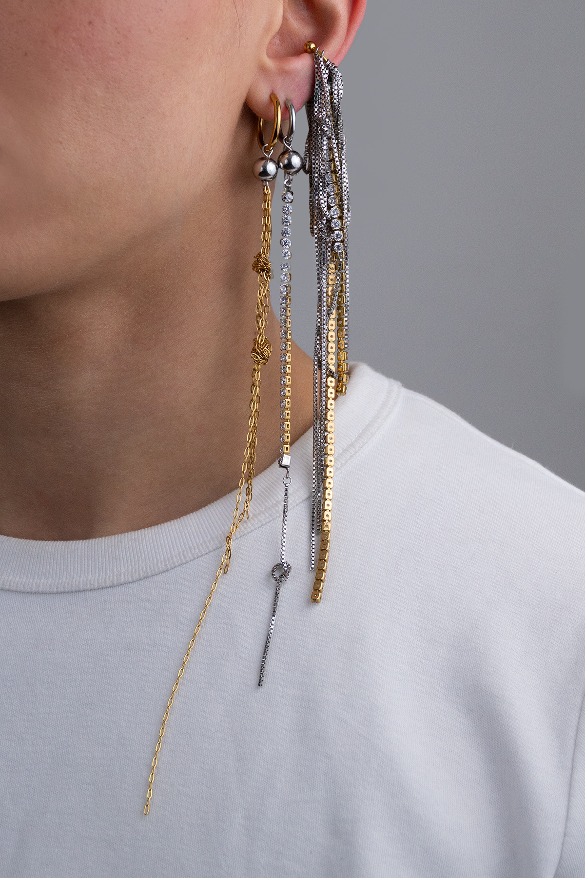 Earcuff en acier inoxydable. Il est composé d’un anneau doré et d’une multitude de chaines argentées de différentes longueurs et de chaines en strass.